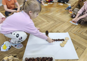 Na zdjęciu widzimy dziewczynkę, która układa kasztana tworząc karmnik dla ptaków z materiału przyrodniczego.