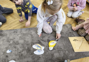 Na ilustracji widzimy dziewczynkę, która z puzzli botanicznych układa ogon.