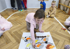 Na zdjęciu widzimy dziewczynkę, która kładzie wykonanego ptaszka na karmniku z materiału przyrodniczego.