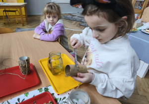 Na zdjęciu widzimy dziewczynkę, która na rolkę po papierze toaletowym nakłada trochę miodu.