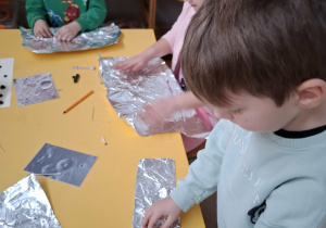 dzieci wyklejają karton folią aluminiową