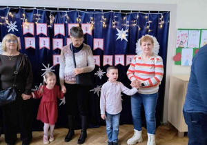 Zdjęcie przedstawia chłopca i dziewczynkę trzymających za ręce swoje babcie.