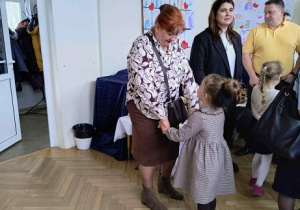 Zdjęcie przedstawia kobietę trzymającą dziewczynkę za ręce.