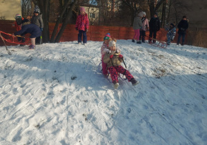 Na zdjęciu dwoje dzieci zjeżających z górki na sankach