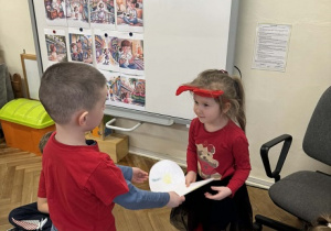 Zdjęcie przedstawia chłopca wręczającego dziewczynce obrazek w kształcie serca.