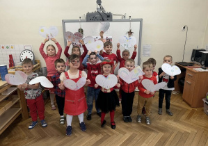 Zdjęcie przedstawia dzieci stojące w grupie, trzymające papierowe serca.