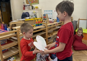 Zdjęcie przedstawia chłopca wręczającego chłopcu obrazek w kształcie serca.