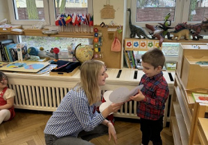 Zdjęcie przedstawia kobietę wręczającą chłopcu obrazek w kształcie serca.