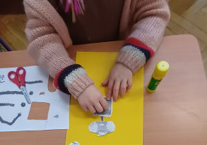 Dziecko siedzi przy stole i nakleja części robota.