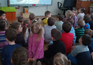 Dzieci siedzą i oglądają bajkę na tablicy interaktywnej.