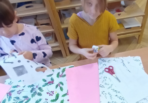Dzieci siedzą przy stole i wycinają elementy robotów.
