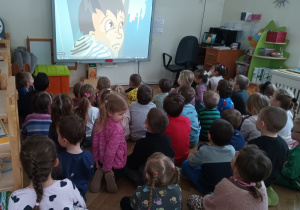Dzieci siedzą i oglądają bajkę na tablicy interaktywnej.