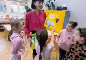 Pani stoi a dzieci wręczają jej laurkę.