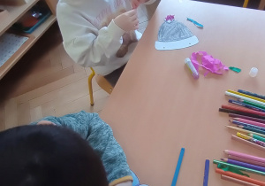 Dzieci siedzą i ozdabiają czapki i rękawiczki.