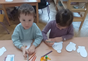 Dzieci siedzą i ozdabiają czapki i rękawiczki.