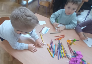 Dzieci siedzą i ozdabiają czapki i rękawiczki.