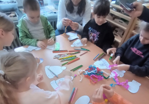 Dzieci siedzą i ozdabiają czapki i rękawiczki.