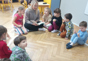 Dzieci siedzą i słuchają czytanej przez panią bajki.