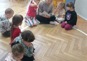 Dzieci siedzą i słuchają czytanej przez panią bajki.