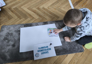 Dziecko przykleja ilustracje na plakat.