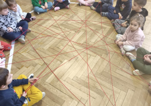 dzieci siedzące w kole i za pomocą włóczki dzieci tworzą sieć