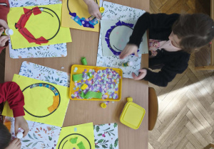 Na zdjęciu widzimy dzieci, które tworzą prace plastyczne - balon z wykorzystaniem kolorowych kółek konfetti i bibuły.