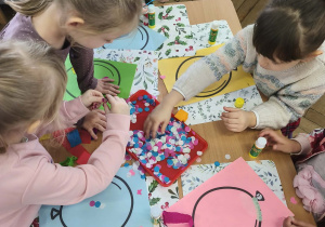 Na zdjęciu widzimy dzieci, które tworzą prace plastyczne - balon z wykorzystaniem kolorowych kółek konfetti i bibuły.
