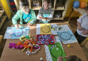Na zdjęciu widzimy dzieci, które tworzą prace plastyczne - balon z wykorzystaniem kolorowych kółek konfetti i bibuły.