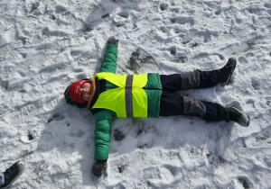 Na zdjęciu widzimy dziecko, które robi aniołka na śniegu.