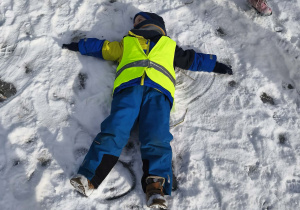 Na zdjęciu widzimy dziecko, które robi aniołka na śniegu.