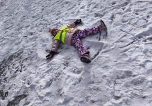 Na zdjęciu widzimy dziecko, które robi aniołka na śniegu.