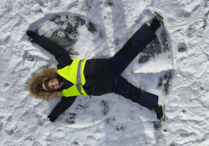 Na zdjęciu widzimy dziecko, które robi aniołka na śniegu.
