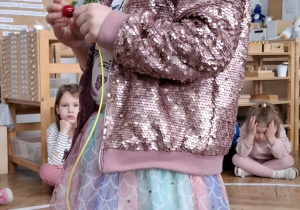 dziewczynka w różowej koronie nawleka korale na sznurek