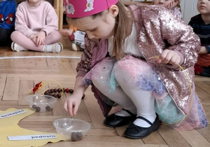 dziewczynka w różowej koronie nawleka korale na sznurek