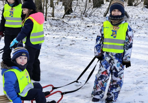 na zdjęciu starszy chłopiec ciągnie na sankach młodszego kolegę