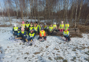 Grupa dzieci siedząca na pniu i sankach podczas penetracji zimowego lasu