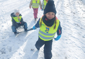 dziewczynka ciągnąca koleżankę na sankach