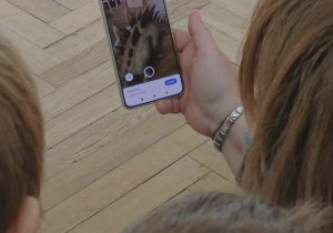 Nauczyciel pokazuje na telefonie obraz dinozaura 3d