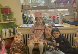 Zdjęcie przedstawia dzieci siedzące wokół dziewczynki. Dziewczynka siedzi na krześle i ma koronę na głowie.