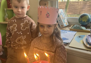 Zdjęcie przedstawia dziewczynka obok tortu z zapalonymi świeczkami.