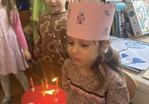 Zdjęcie przedstawia dziewczynkę podczas dmuchania świeczek na torcie.