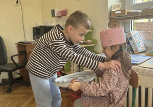 Zdjęcie przedstawia chłopca opierajacego ręce na ramionach dziewczynki, podczas składania życzeń.