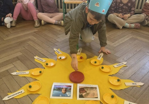 Zdjęcie przedstawia chłopca wkładającego świeczkę w tort na słoneczku urodzinowym.