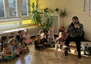 Zdjęcie przedstawia dzieci siedzące na podłodze, podczas rozmowy z mężczyzną.