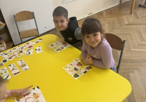 Zdjęcie przedstawia dzieci siedzące przy stole, na których poukładane są obrazki.