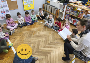 Na zdjęciu widzimy grupkę dzieci, które słuchają czytania mamy Alicji.