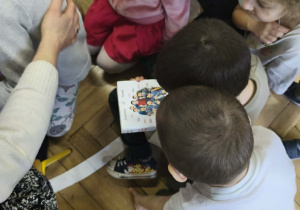 Na zdjęciu widzimy dzieci, które oglądają książkę i jej okładkę.