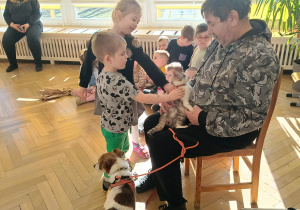 Zdjęcie przedstawia mężczyznę trzymającego kota, obok stoi pies. Do mężczyzny podeszły dzieci, aby pogłaskać kota.