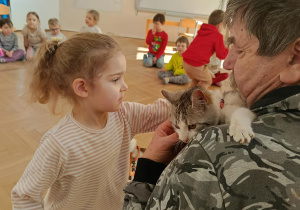 Zdjęcie przedstawia dziewczynkę, która głaszcze kota trzymanego przez mężczyznę.