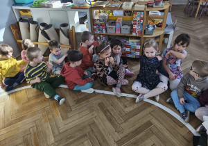 Na zdjęciu widzimy dzieci, które siedzą na podłodze w parach i pokazują, że kaszlą pod wpływem wąchania dymu papierosowego.